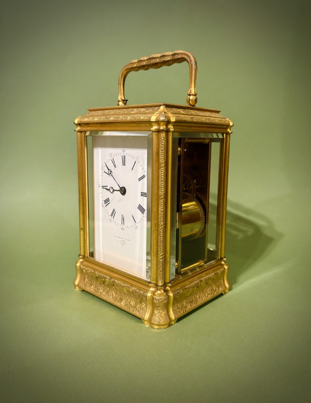 An antique rectangular French carriage clock featuring a gilt brass case with engraved foliage, glass side panels, a top carrying handle, and a white enamel dial displaying Roman numerals. View III