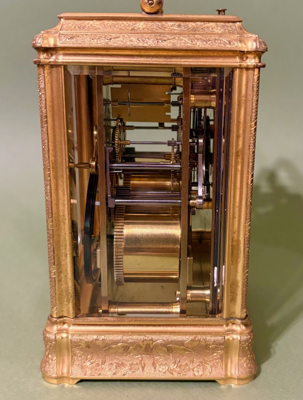 An antique rectangular French carriage clock featuring a gilt brass case with engraved foliage, glass side panels, a top carrying handle, and a white enamel dial displaying Roman numerals. View V