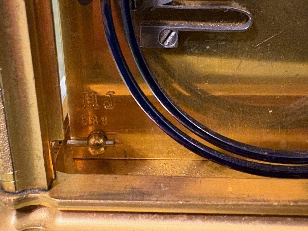 An antique rectangular French carriage clock featuring a gilt brass case with engraved foliage, glass side panels, a top carrying handle, and a white enamel dial displaying Roman numerals. View VII