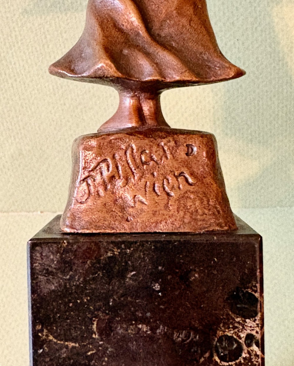 A patinated bronze figurine depicting a young farmer girl holding a rake, mounted on a dark marble pedestal base. View V