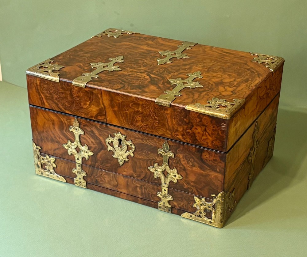 An open Victorian burr walnut dressing case featuring brass mounts, green velvet lining, silver-topped glass jars, vanity tools, and a pull-out lower drawer. View III