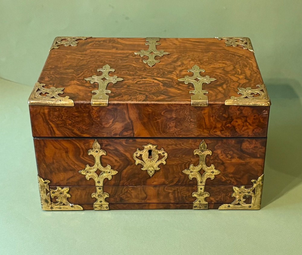 An open Victorian burr walnut dressing case featuring brass mounts, green velvet lining, silver-topped glass jars, vanity tools, and a pull-out lower drawer. View VI