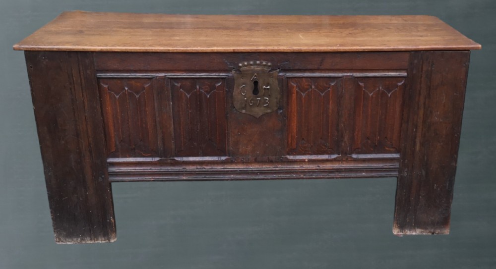 A 17th-century dark oak coffer with carved linenfold front panels and a central metal escutcheon dated 1673.