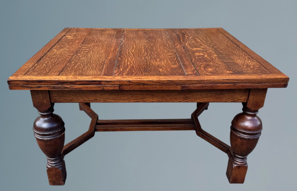 A rectangular warm brown oak draw-leaf dining table featuring heavy bulbous turned legs, low stretchers, and a quarter-sawn timber grain top.