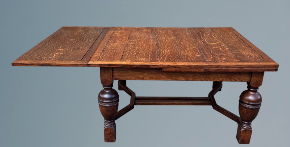 A rectangular warm brown oak draw-leaf dining table featuring heavy bulbous turned legs, low stretchers, and a quarter-sawn timber grain top. View III