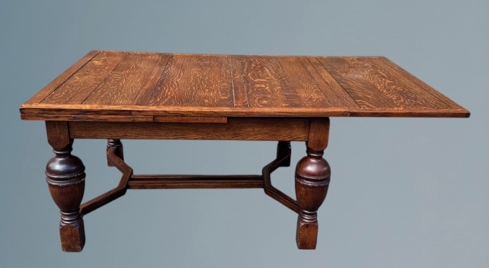 A rectangular warm brown oak draw-leaf dining table featuring heavy bulbous turned legs, low stretchers, and a quarter-sawn timber grain top. View IV