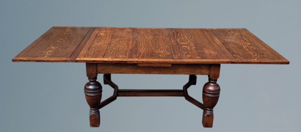 A rectangular warm brown oak draw-leaf dining table featuring heavy bulbous turned legs, low stretchers, and a quarter-sawn timber grain top. View V