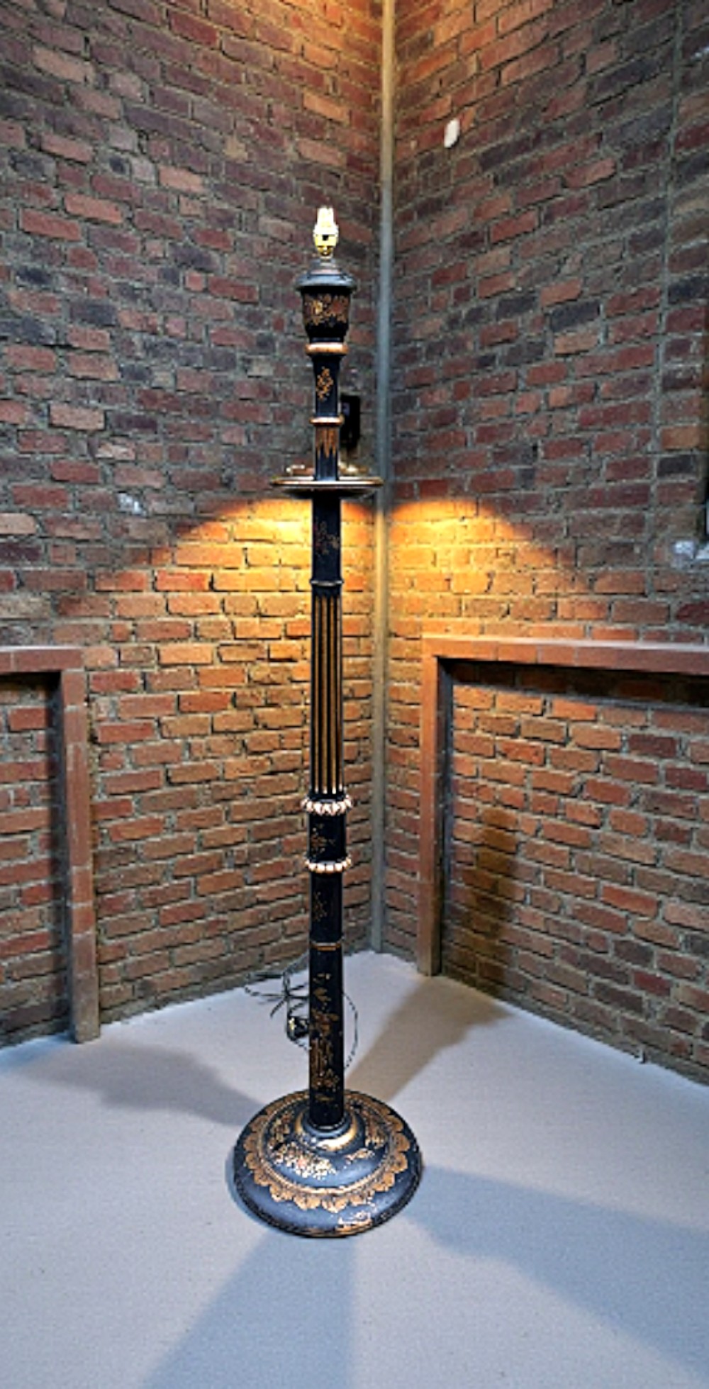 A tall black lacquered standard lamp decorated with hand-painted gold Chinoiserie motifs and a turned central column set on a circular pedestal base.