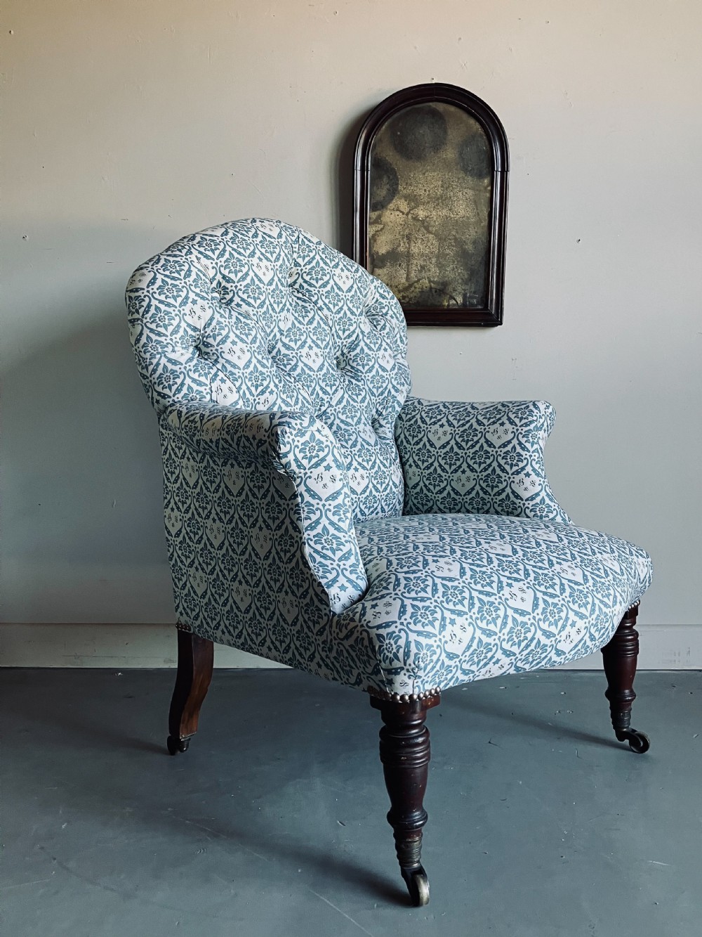 A Victorian button-backed armchair upholstered in a blue and white botanical pattern with turned front legs on brass castors.