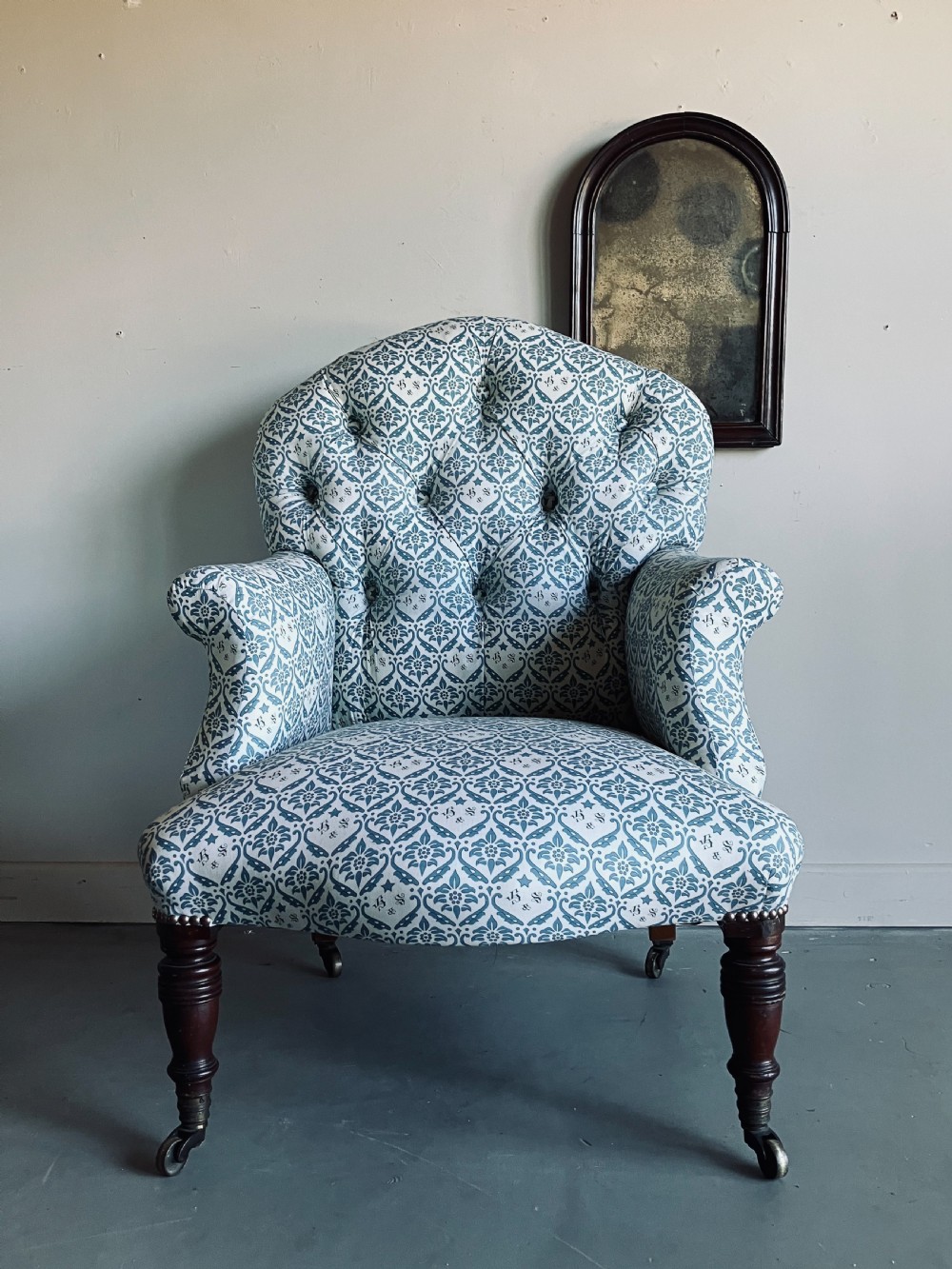 A Victorian button-backed armchair upholstered in a blue and white botanical pattern with turned front legs on brass castors. View II