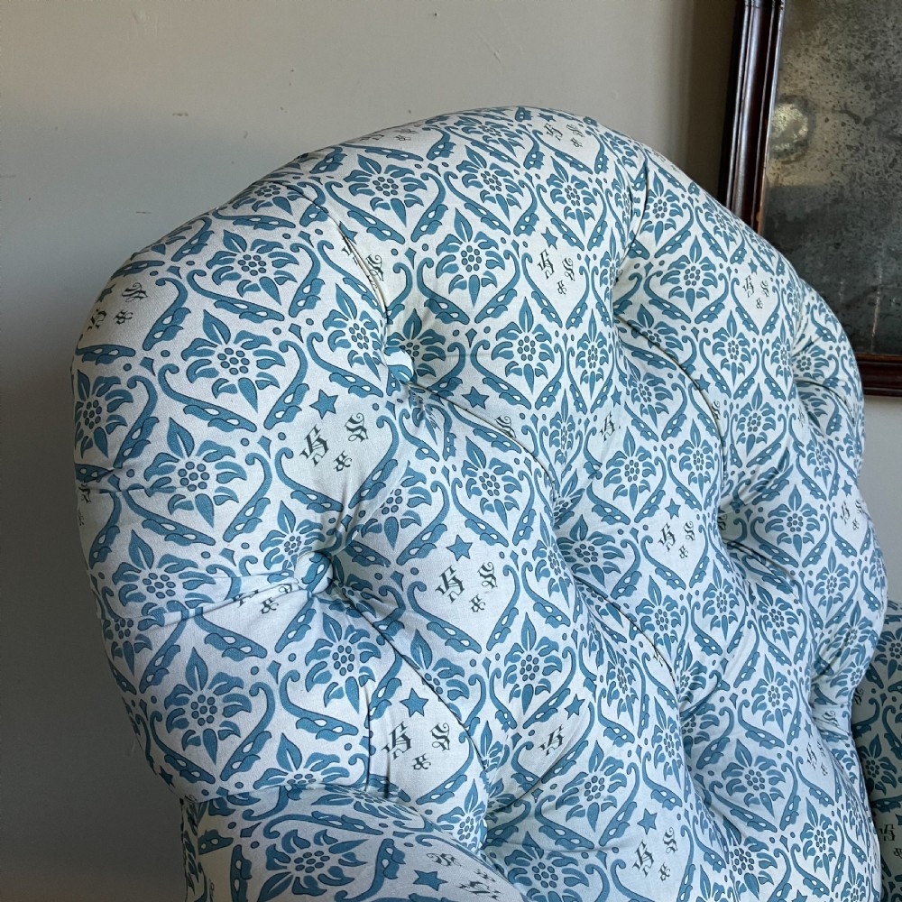 A Victorian button-backed armchair upholstered in a blue and white botanical pattern with turned front legs on brass castors. View III