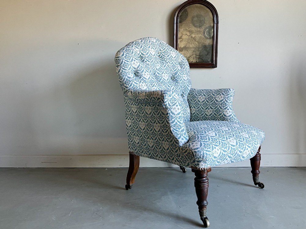 A Victorian button-backed armchair upholstered in a blue and white botanical pattern with turned front legs on brass castors. View VI