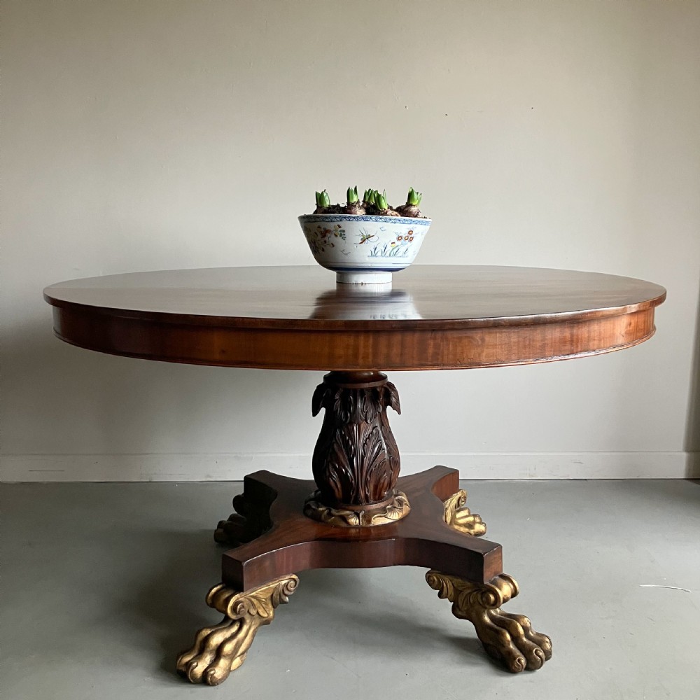 A circular mahogany centre table featuring a carved acanthus pedestal column and a quadform base with gilded claw feet.