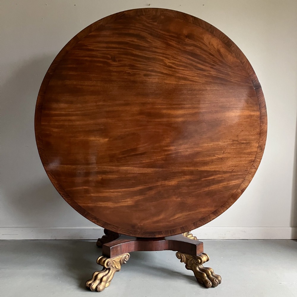 A circular mahogany centre table featuring a carved acanthus pedestal column and a quadform base with gilded claw feet. View II