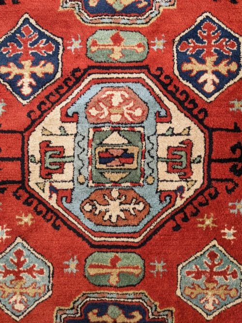 fig 1. An antique hand-knotted Caucasian Kazak wool carpet featuring three geometric medallions along a terracotta red field, enclosed by light blue and cream patterned borders.