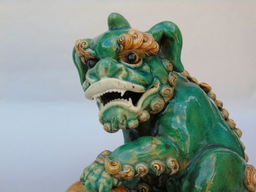 fig 1. A pair of 19th-century Chinese Sancai glazed ceramic guardian lions with green and amber glazes, one resting a paw on a ball and the other on a cub.