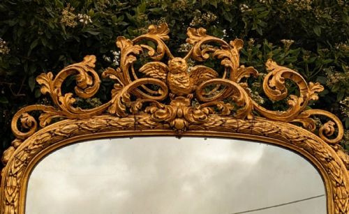 fig 1. An ornate floor-standing cheval mirror framed in gold giltwood with carved cresting and turned supports.