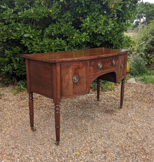 fig 1. A Regency period mahogany sideboard featuring turned legs on brass castors, central drawer, flanking cupboard doors, and circular brass ring handles.