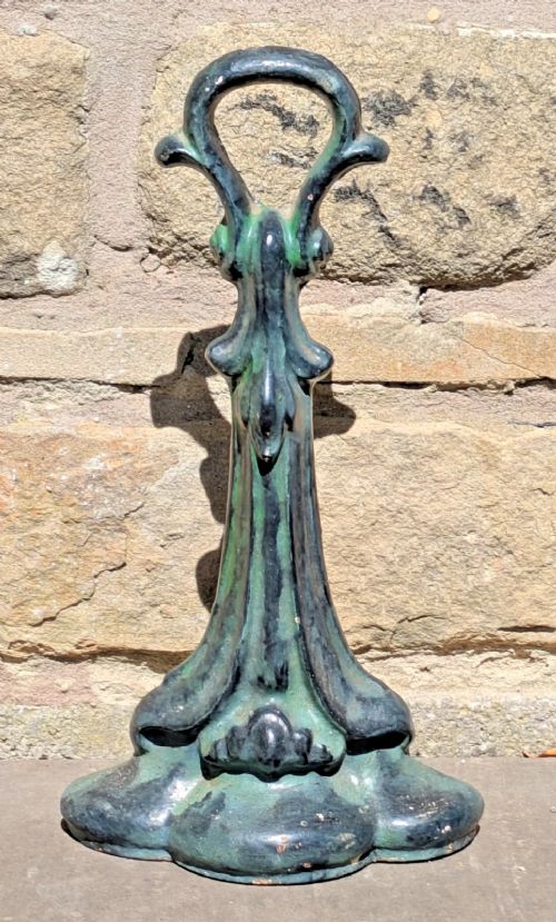 An Art Nouveau cast iron doorstop featuring a vertical stem with organic leaf motifs, a loop handle at the top, and a green patinated finish.