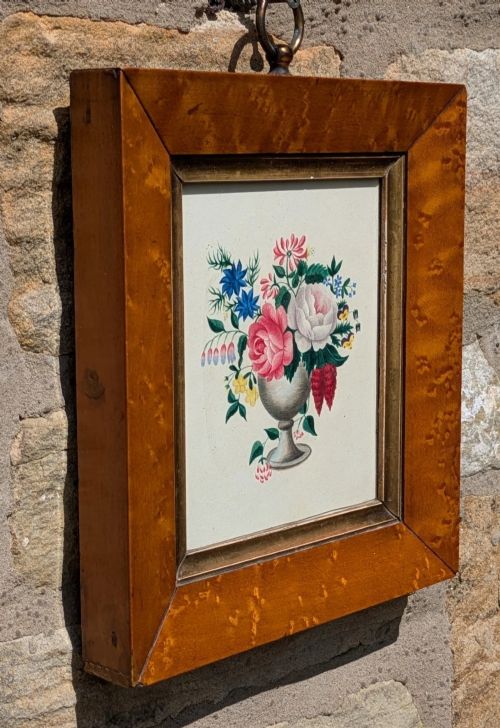 fig 1. A framed Regency watercolour painting depicting a vibrant floral bouquet in an urn, set within a wide burr wood frame featuring a brass suspension ring.