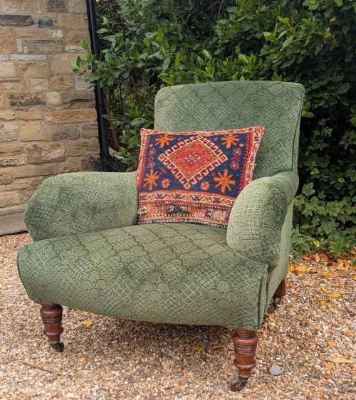 fig 1. A low-slung 19th-century Howard style armchair upholstered in patterned green fabric with turned mahogany front legs and brass castors.