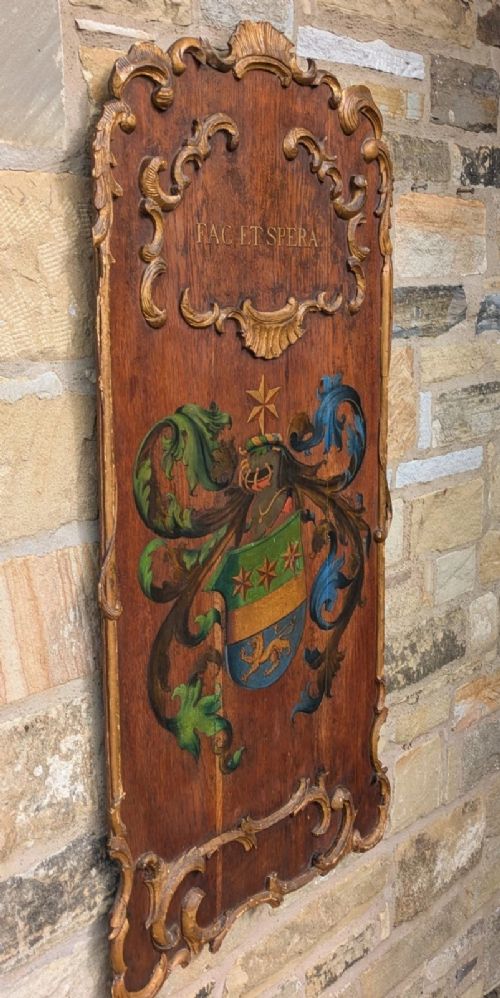 A rectangular carved oak wall plaque featuring a hand-painted heraldic coat of arms, gilt scroll moulding, and a Latin motto. View IV