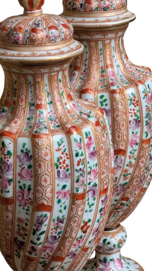 A pair of hand-painted porcelain lidded vases featuring fluted bodies, intricate floral motifs, geometric orange bands, and gilded details on square pedestals. View VIII