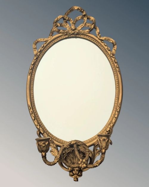 fig 1. A matching pair of oval giltwood girandole wall mirrors featuring ribbon cresting and twin candle sconces at the base.
