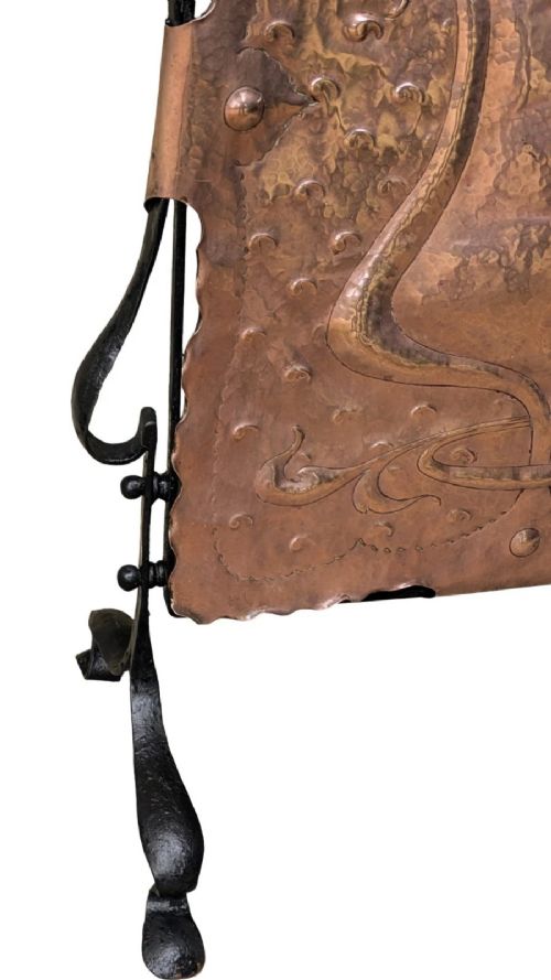 An Arts and Crafts fire screen constructed from a hand-hammered copper central panel with raised relief decoration, held within a black wrought iron scrollwork frame. View IV