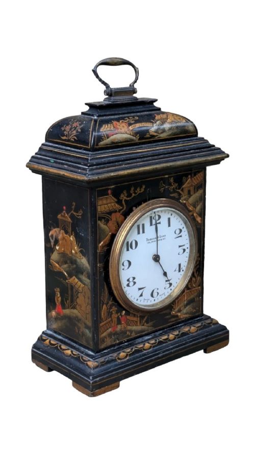 fig 1. A black lacquered Regency style mantel clock decorated with gold hand-painted Chinoiserie landscapes, featuring a white circular dial with Arabic numerals and a top brass handle.