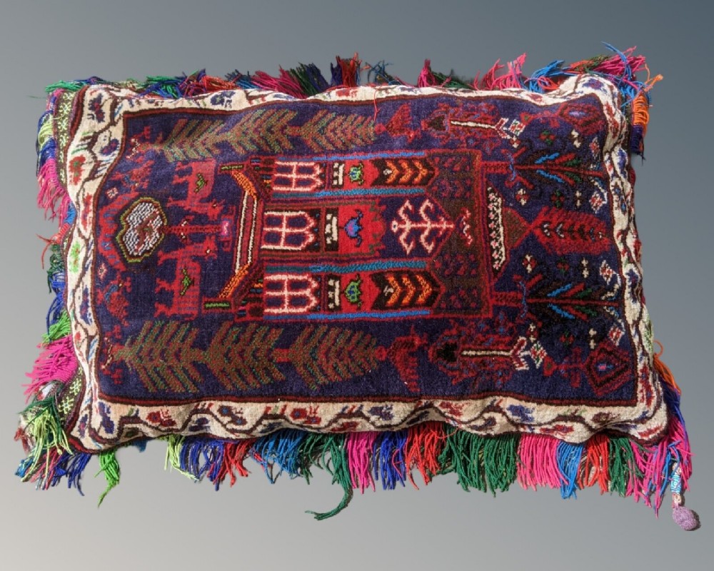 A rectangular hand-woven wool cushion crafted from an antique tribal bag face with geometric motifs, a navy blue ground, and multicoloured fringe edges.