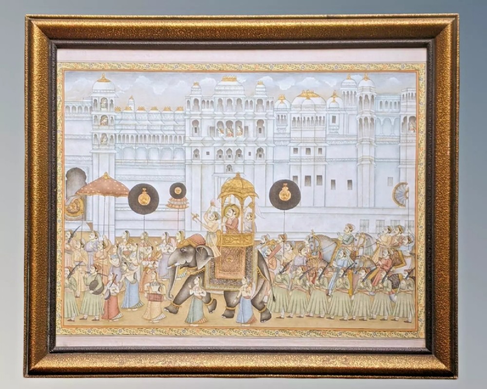 Framed Indian silk painting displaying a royal procession featuring a Maharajah on an elephant with attendants and horses against a white palace backdrop.