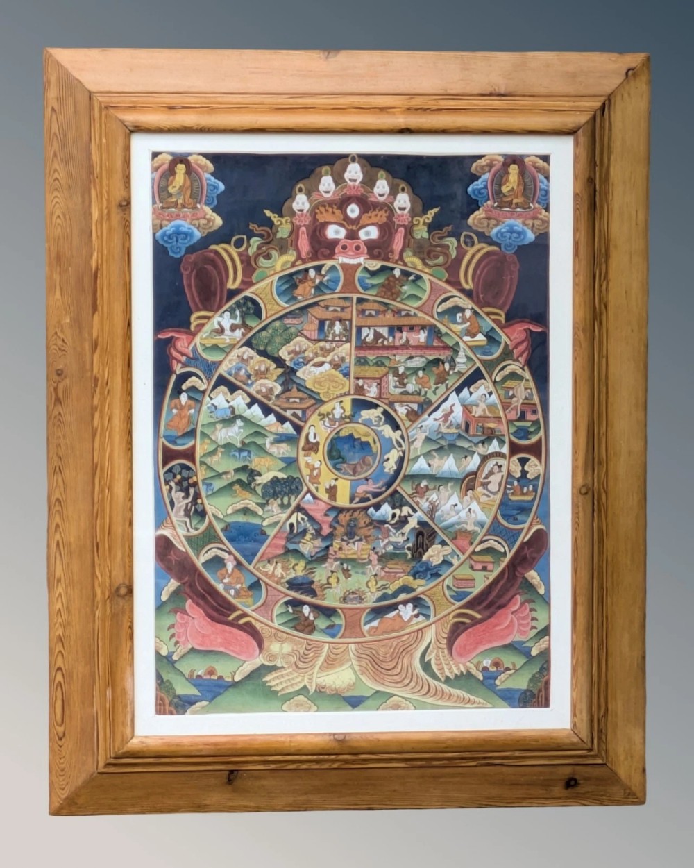 A handpainted Tibetan Wheel of Life Thangka artwork featuring intricate Buddhist symbols encased in a natural pine wood frame.