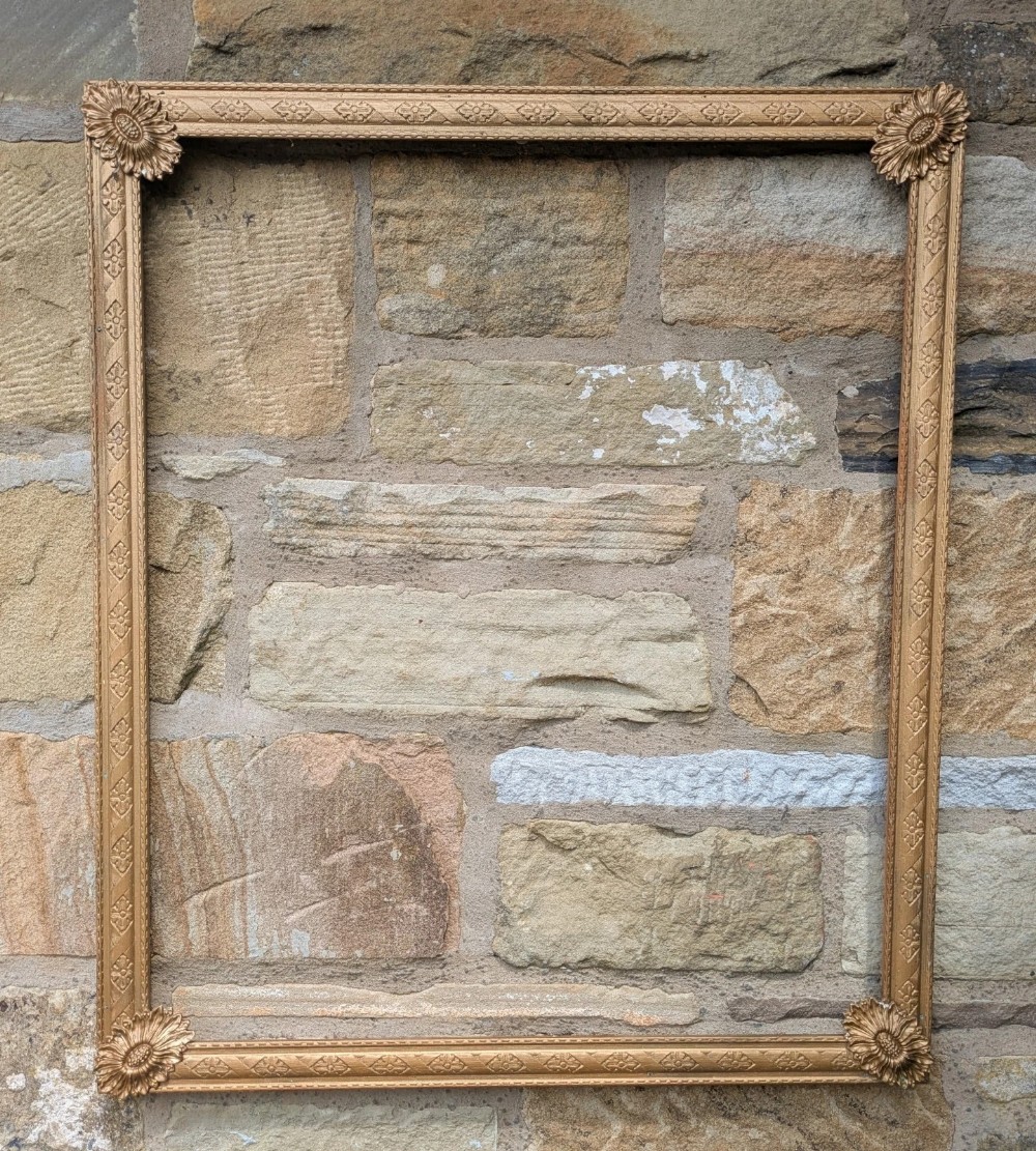 A rectangular antique gilt picture frame featuring carved rosette corner details and decorative patterned moulding.
