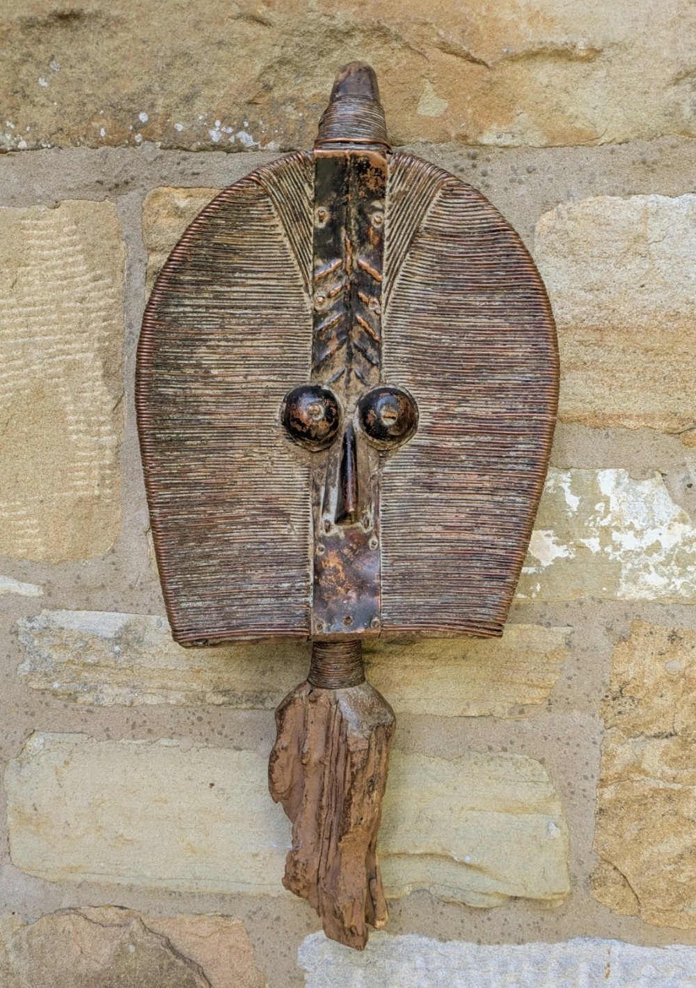 A carved wooden Mahongwe reliquary guardian figure from Gabon wrapped in copper wire with metal sheet accents.