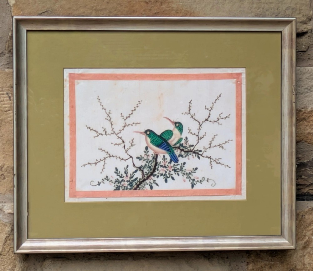 A framed Chinese watercolour painting depicting two green and blue birds perched on a flowering branch set within an olive green mount.