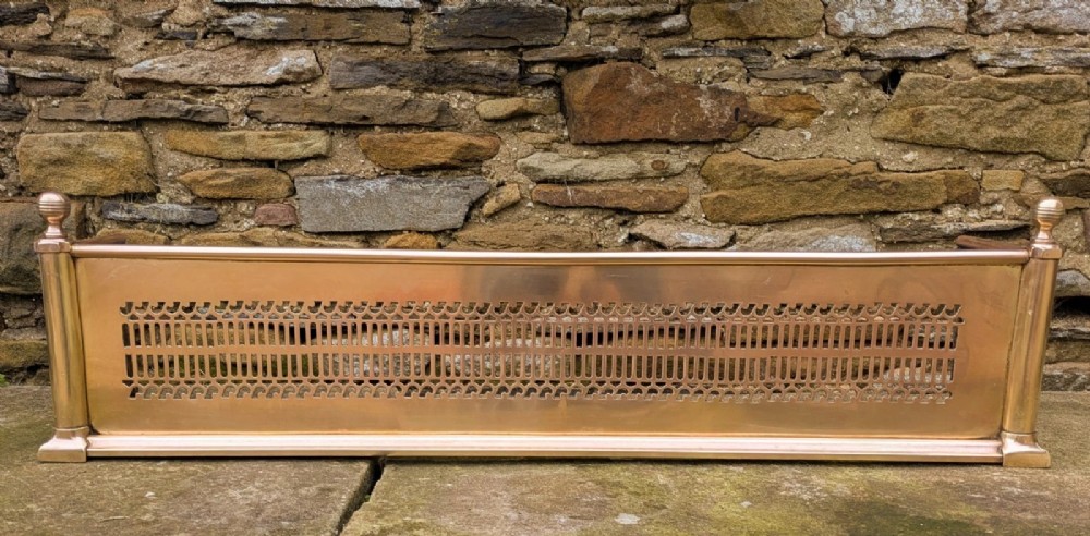 A 19th-century polished brass fire fender featuring a central band of pierced geometric fretwork and corner posts topped with ball finials.