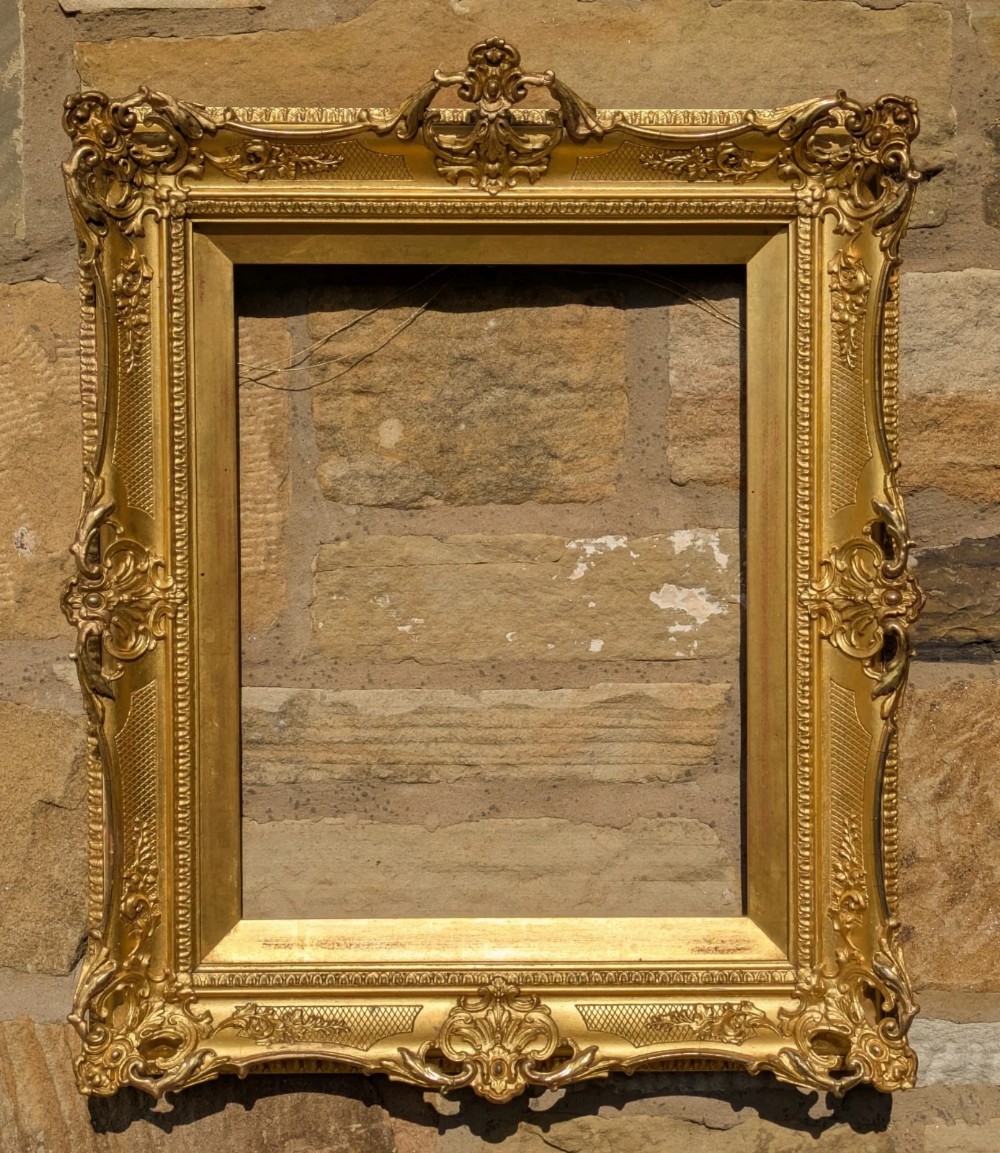 A 19th-century gold leaf swept picture frame with ornate scrollwork corners, floral relief moulding, and cross-hatched details.