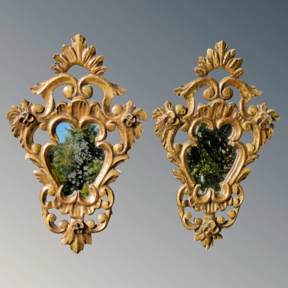 A pair of French carved giltwood wall mirrors with intricate acanthus leaf cresting and pierced scrollwork framing central glass panels.