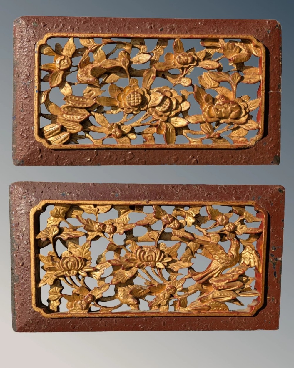 A pair of rectangular Chinese carved wood panels featuring openwork floral and bird motifs finished in gold gilding and framed by textured red lacquer borders.