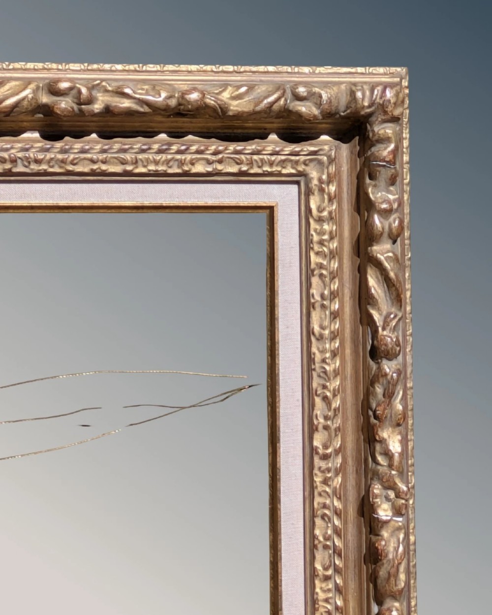 A rectangular carved gilt wood picture frame with an inner neutral linen slip and a central brass plaque along the lower edge. View III