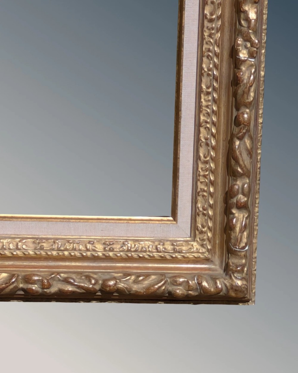 A rectangular carved gilt wood picture frame with an inner neutral linen slip and a central brass plaque along the lower edge. View V