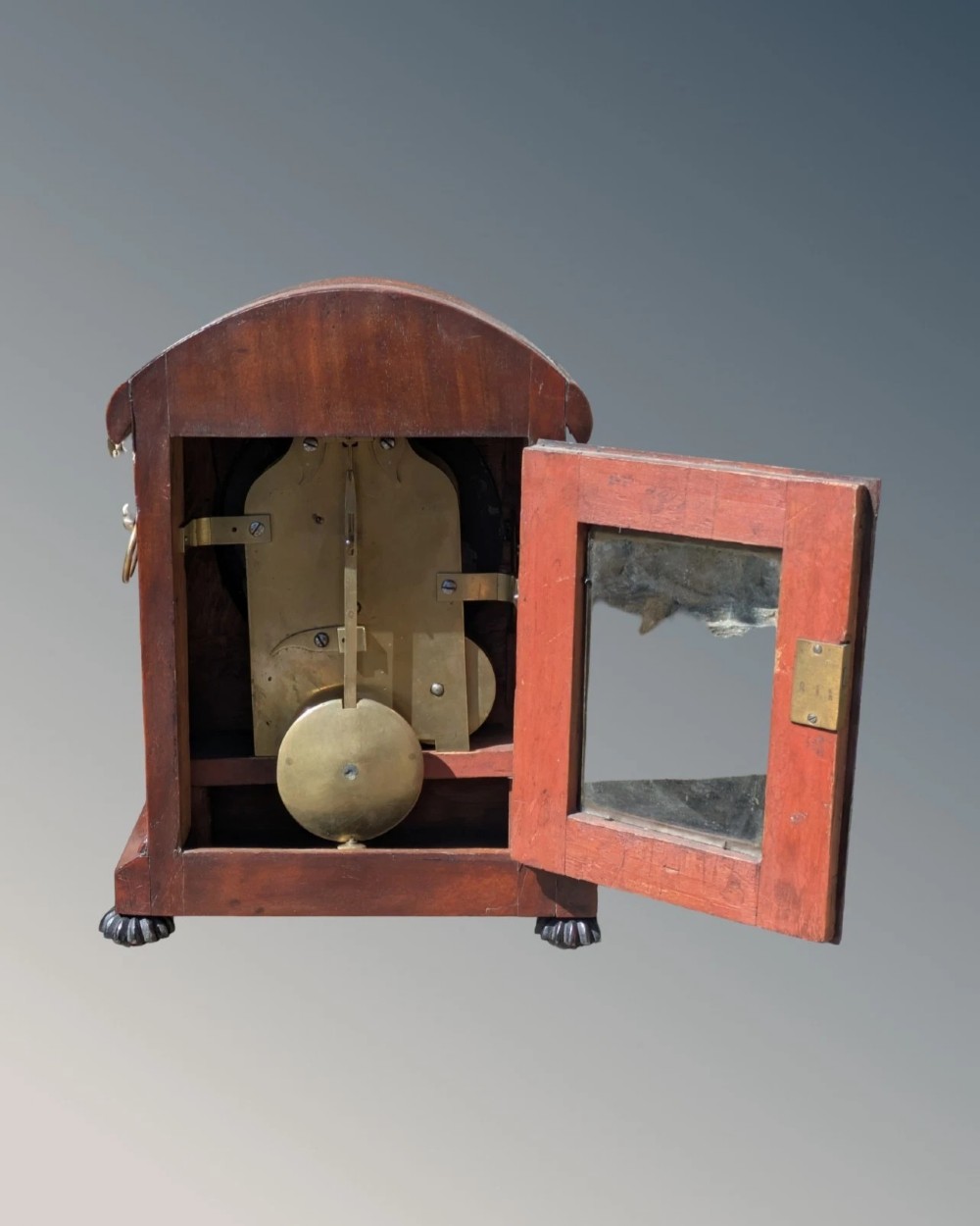 A 19th-century mahogany bracket clock featuring a carved curved pediment, a white circular dial with Roman numerals, side ring handles, and carved bracket feet. View VIII