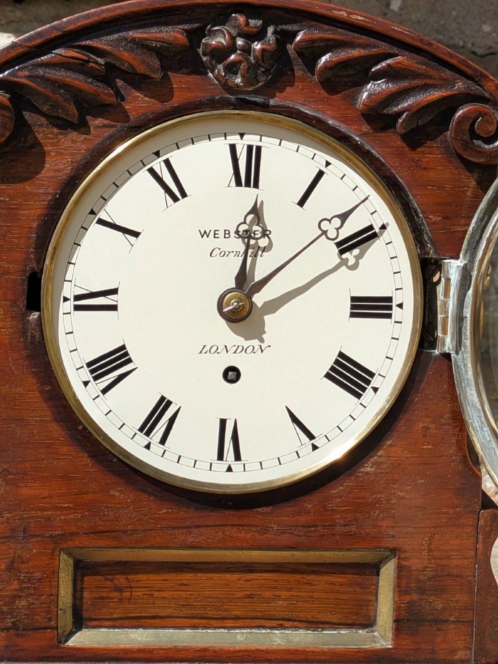 A 19th-century mahogany fusee bracket clock with carved foliate cresting, a brass finial, a white circular dial with Roman numerals, and small brass ball feet. View III