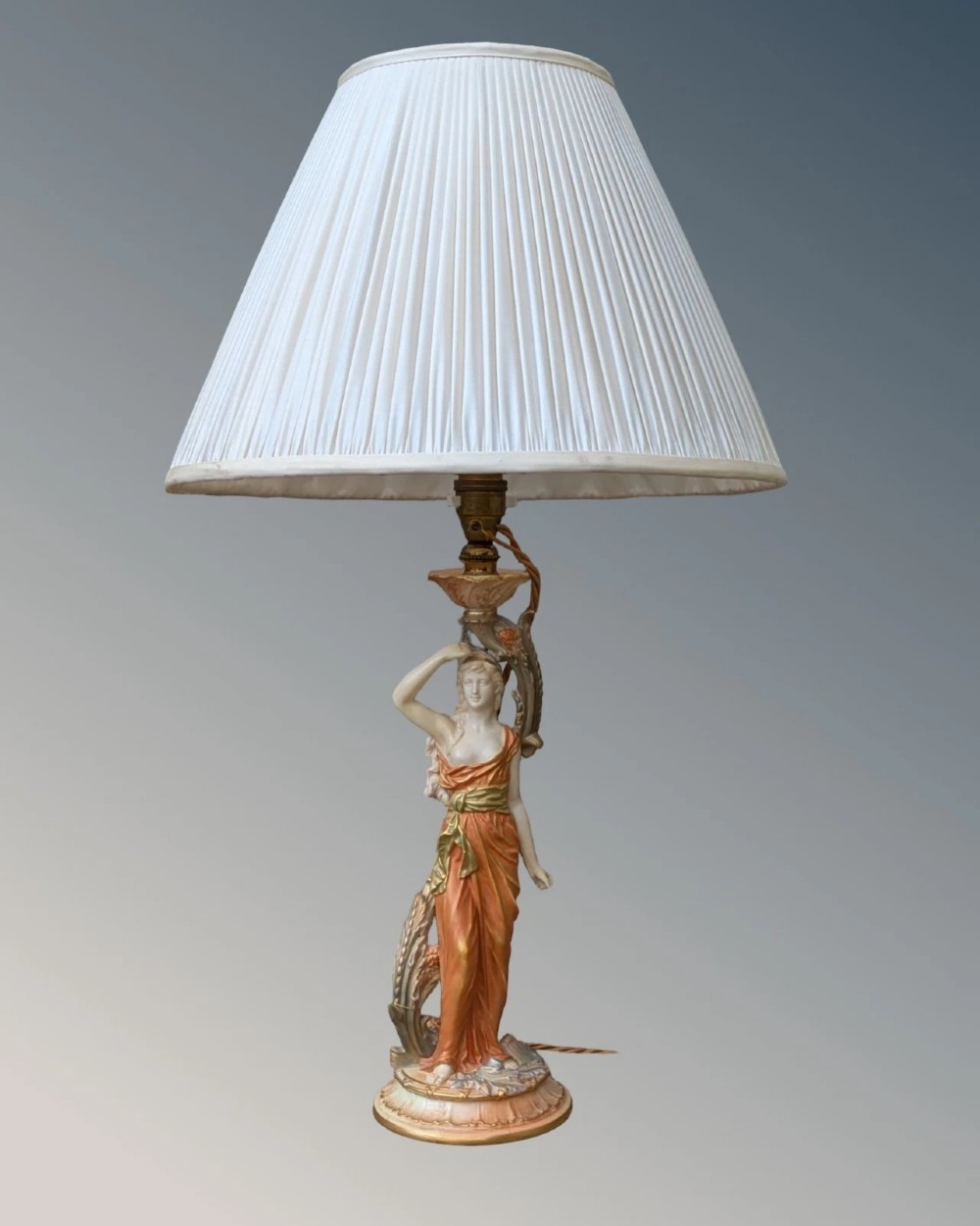A Royal Worcester porcelain table lamp featuring a sculpted classical female figure in terracotta drapery beneath a pleated white shade.