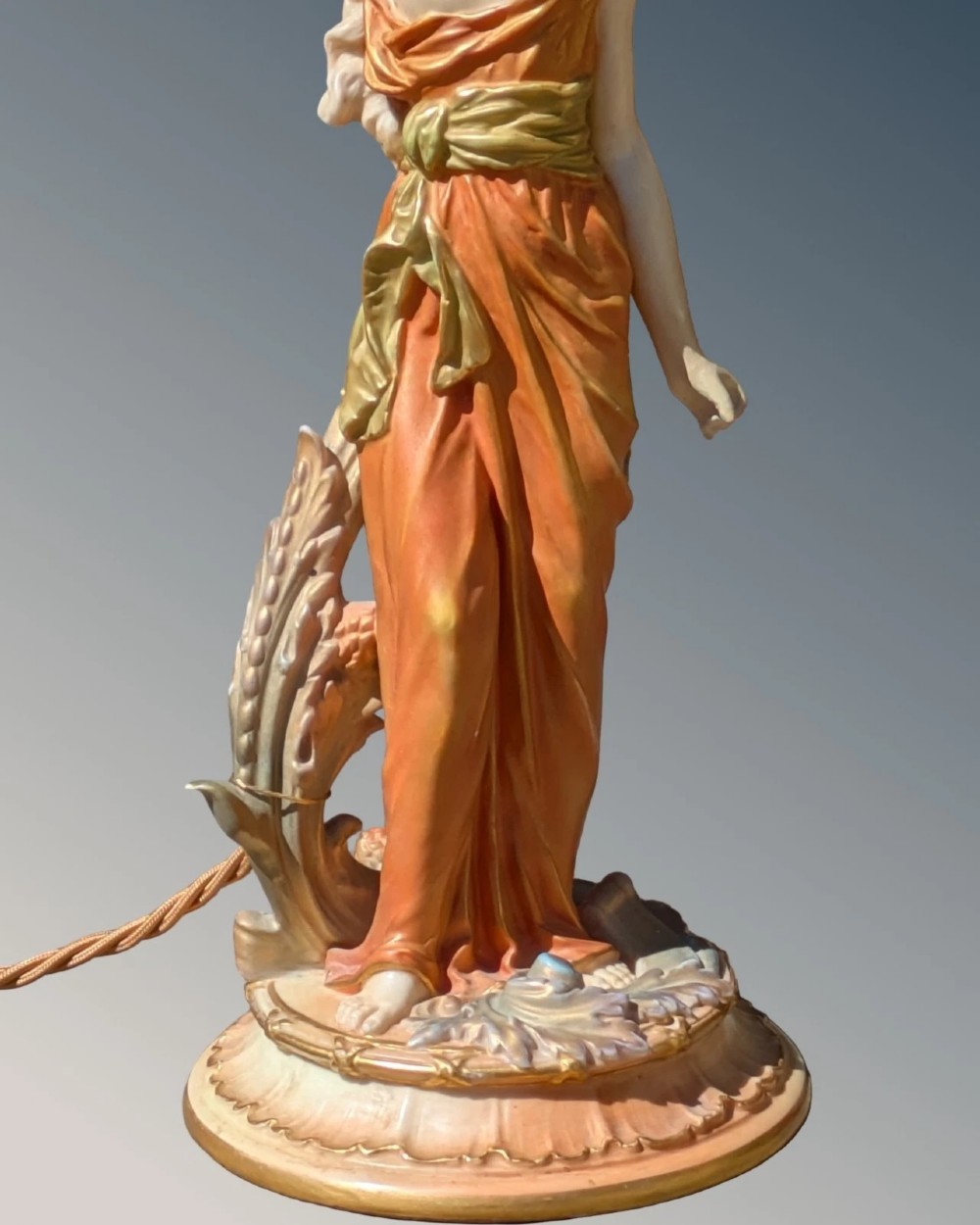 A Royal Worcester porcelain table lamp featuring a sculpted classical female figure in terracotta drapery beneath a pleated white shade. View V