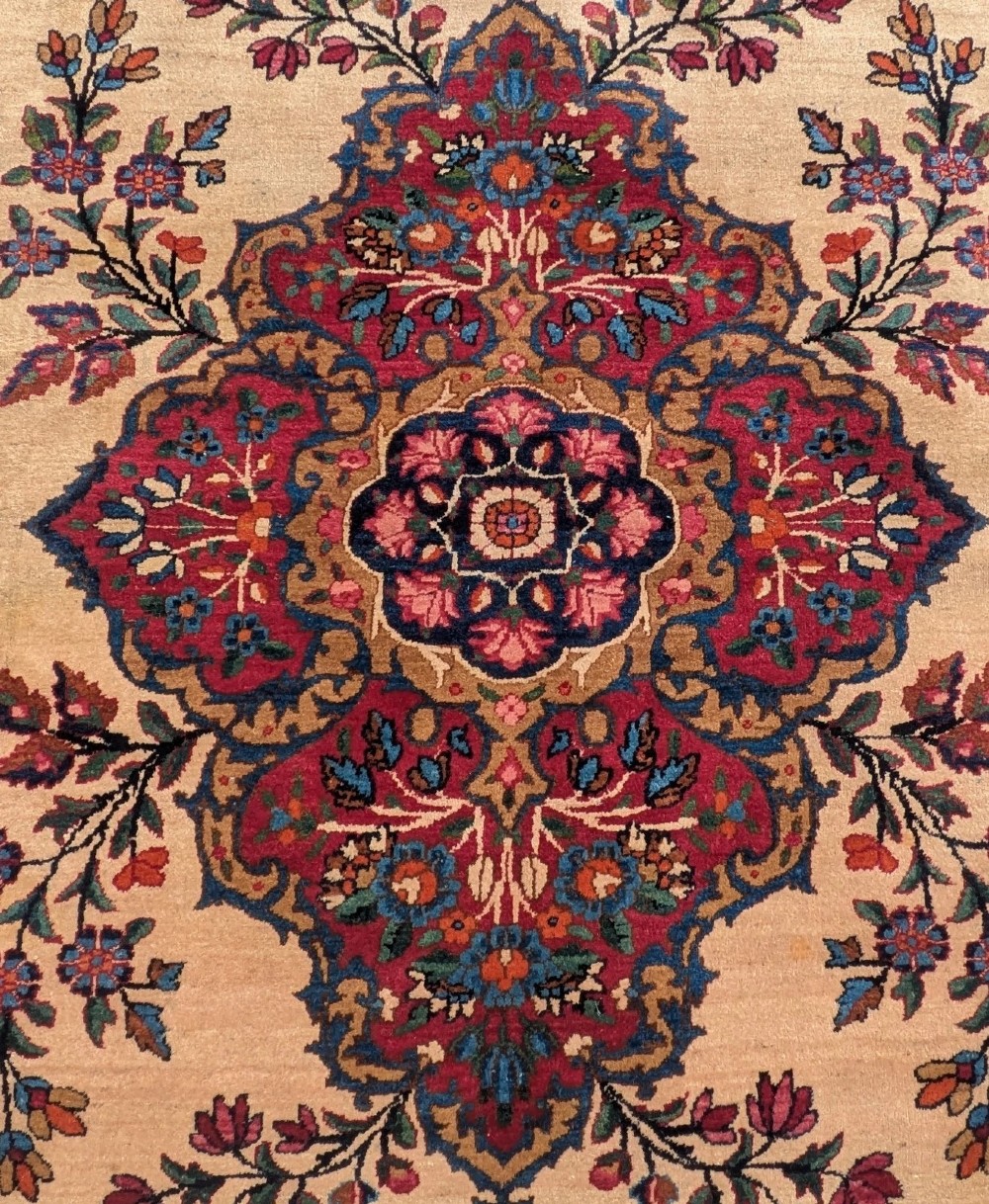 An antique room-sized Kirman Persian carpet featuring a complex central floral medallion on an ivory field surrounded by floral borders in red, navy blue, and gold. View IV