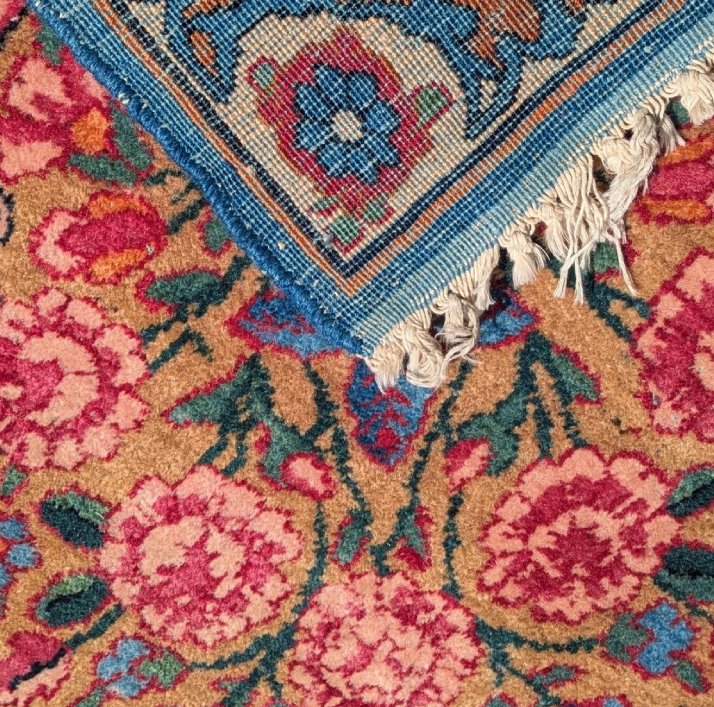 An antique room-sized Kirman Persian carpet featuring a complex central floral medallion on an ivory field surrounded by floral borders in red, navy blue, and gold. View VII
