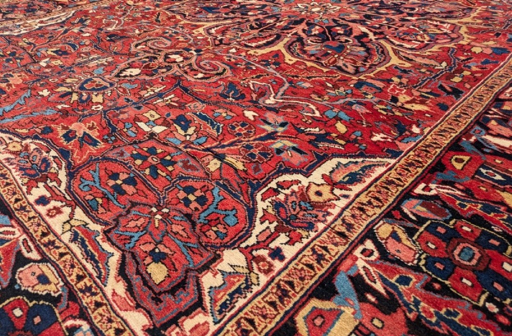 An antique hand-knotted Ahar Heriz wool carpet featuring a large central floral medallion surrounded by detailed vine motifs in rust red, navy blue, and ivory tones. View III