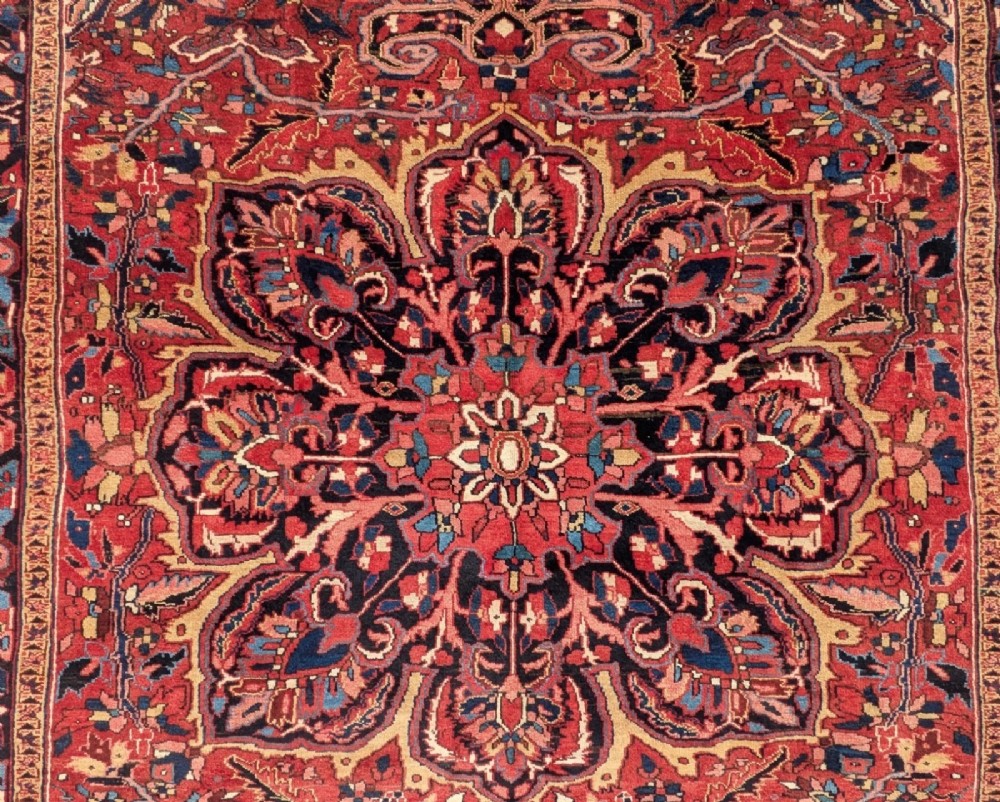 An antique hand-knotted Ahar Heriz wool carpet featuring a large central floral medallion surrounded by detailed vine motifs in rust red, navy blue, and ivory tones. View IV